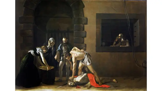 Un cuadro de Caravaggio en el que se ve la decapitación de San Juan Bautista, una mujer está mirando con las manos en la cara, otra mujer prepara una bandeja y un hombre las acompaña. Al fondo se ve a un preso presenciando la escena desde la ventana de su celda.