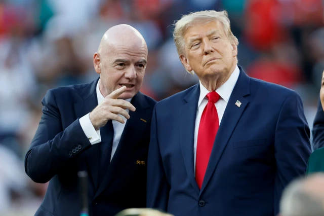 Gianni Infantino, vestido con un camina blanca y corbata y traja oscuro, habla con el presidente de EE.UU. que está a su lado, vestido con una camisa blanca, traje azul oscuro y corbata roja.