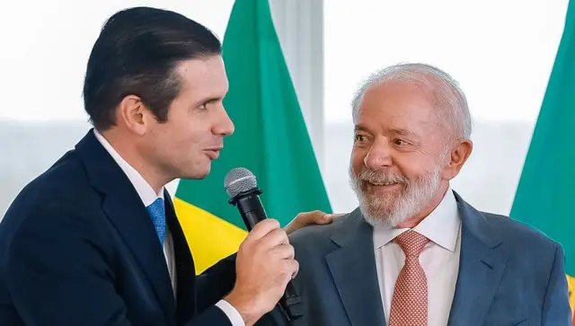 Hugo Motta fala ao microfone com mão no ombro de Lula