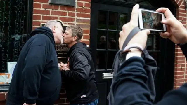 Stonewall Inn önünde öpüşen bir çiftin fotoğrafını çeken bir kamera.