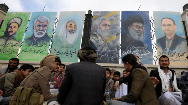 حوثيون يمنيون بالقرب من جدارية تحمل صور شخصيات عسكرية وسياسية ذي ارتباط بجماعات مدعومة من إيران