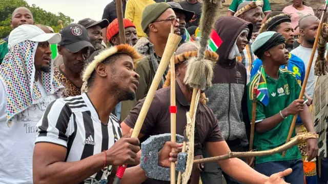 Protesters hold stick and dem dey chant