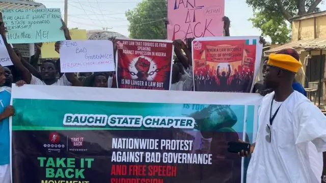 A man wey wear white agbada wit orange beret holding a banner