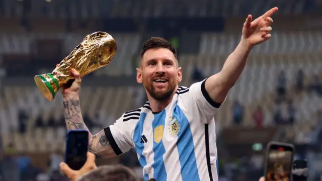 Lionel Messi carrega com uma das mãos o troféu da Copa do Mundo da Fifa de Futebol Masculino em 2022, no Catar