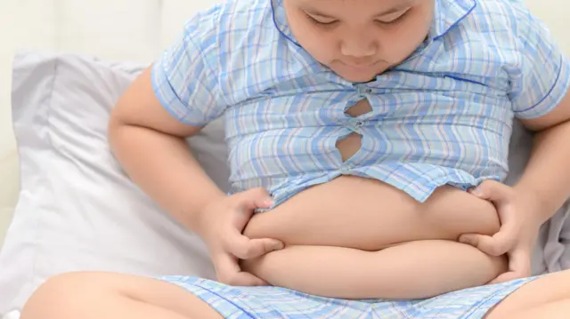 un niño con sobrepeso sosteniéndose el abdomen