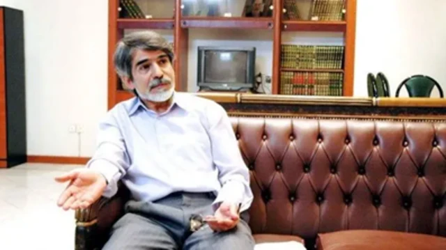 پورنجاتی روی مبل چرمی قهوه ای رنگ نشسته و عینکش را در دست دارد. 