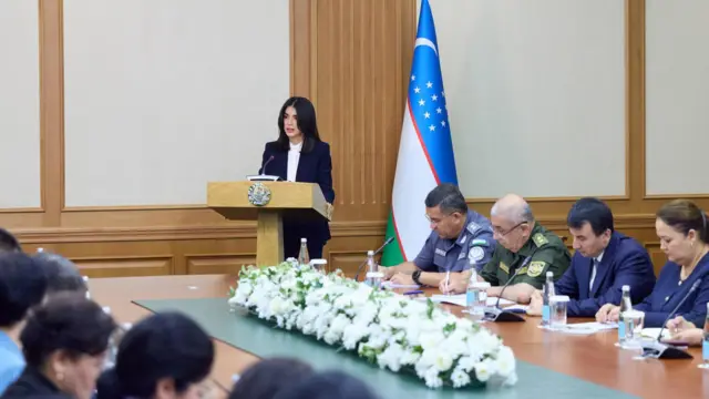 Саида Мирзиёева минбарда нутқ сўзламоқда. Уни эшитиб ўтирган мансабдорлар – Ички ишлар вазири, Бош прокурор ва Бош вазир ўринбосари аниқ кўринган – ўз дафтарларига қайдлар ёзмоқда.