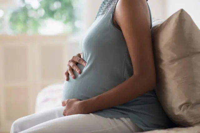 Mulher grávida sentada, de perfil, com a mão na barriga