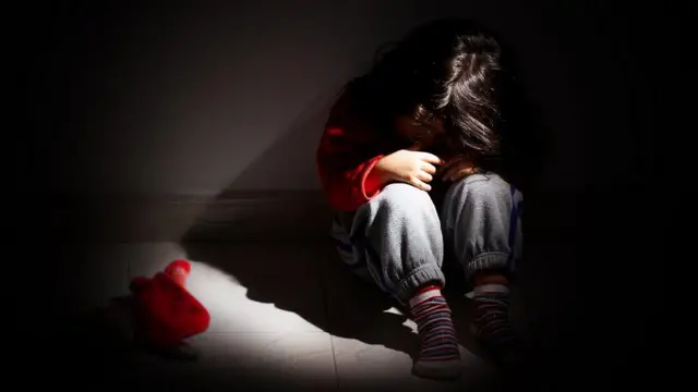 Seorang anak perempuan duduk di kegelapan.