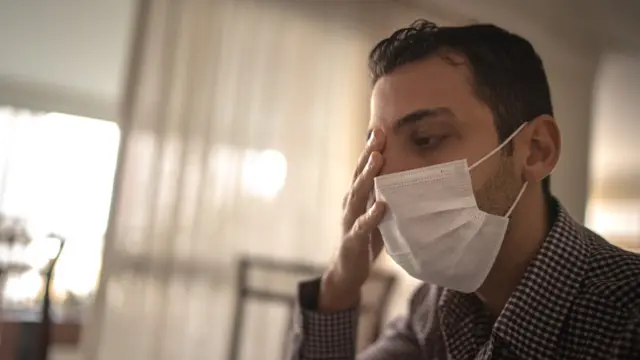 Un homme avec un masque facial se frotte un œil