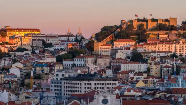 Imagem mostra vista geralcomo fazer retirada no sportingbetPortugal, com vários imóveis, bandeiras do país e o Castelocomo fazer retirada no sportingbetSão Jorge aparecendo