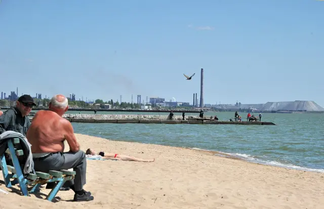 idosos tomam solgratis betsuma praia com um porto ao fundo sob o sol