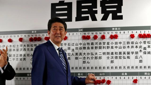 安倍晋三在自民党总部的当选名录前朝着记者咧嘴而笑（22/10/2017）