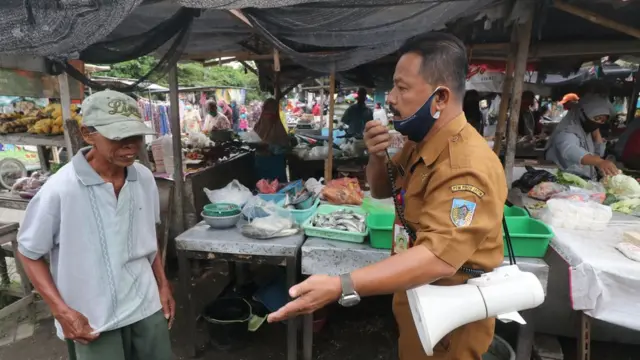 Petugas menegur warga yang tidak menggunakan masker saat sosialisasi Adaptasi Kebiasaan Baru di pasar Sumberejo, Kediri, Jawa Timur, Selasa (21/07).