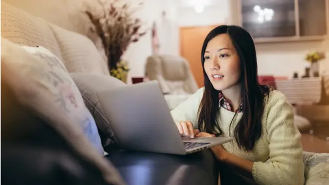 Mulher olha sorrindo para laptop apoiado no sofá da sala