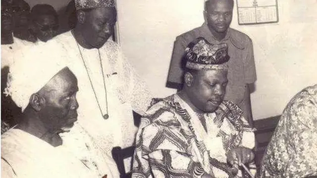 Fajemirokun n kọ iwe, eeyan meji wa ni ẹgbẹ ọtun ati osi rẹ