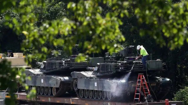 A worker washes one of two M1A1 Abrams tanks that are loaded on rail cars at a rail yard on 2 July in Washington, DC