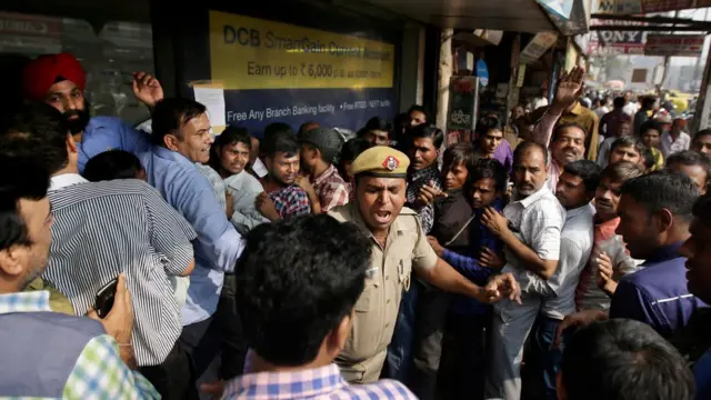 दिल्ली में एक बैंक के बाहर कतार तोड़ने वाले लोगों को डांटता पुलिसमैन