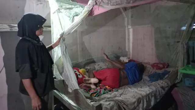 Ngatemi, 59 tahun, dan suami yang terbaring akibat menderita stroke di rumahnya.