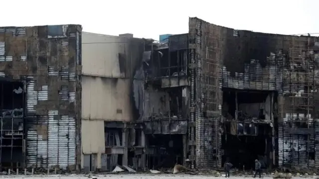 યુદ્ધમાં ક્ષતિગ્રસ્ત થયેલી એક ઇમારત પાસેથી પસાર થતાં કેટલાક લોકો