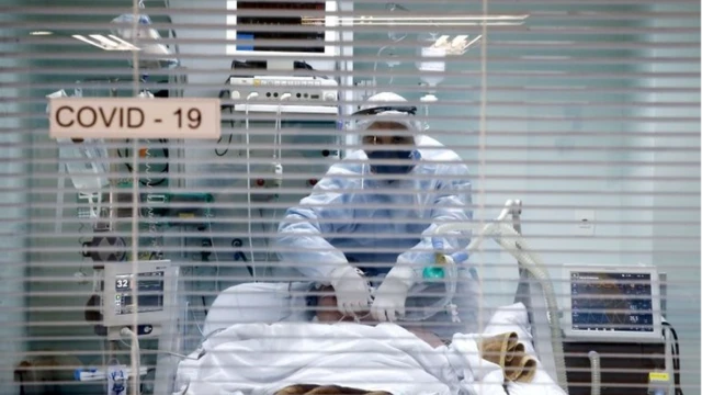 Por trás de persiana em hospital, profissional manipula paciente em maca