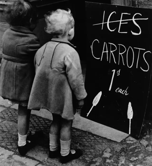 1941లో పిల్లలకు ఐస్ బదులుగా ఒక్కొక్కరికి ఒక్కో క్యారెట్ ఇస్తామని చెప్తున్న బోర్డును చూస్తున్న ఇద్దరు చిన్నారులు