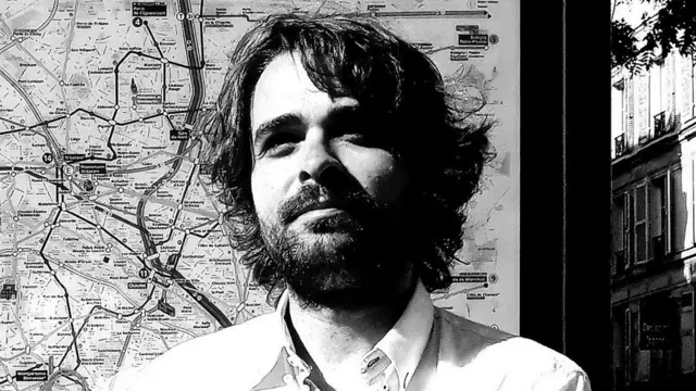 Edgar Cabanas em frente a mapa na rua, olhando para longe com sorriso contido
