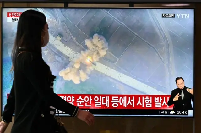 지난 6월 5일 북한이 동해상으로 미사일을 발사한 가운데 한 여성이 관련 소식을 전하는 서울역 TV 앞을 지나가고 있다