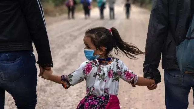 Niña de la mano de dos adultos en una marcha hacia la frontera estadounidense