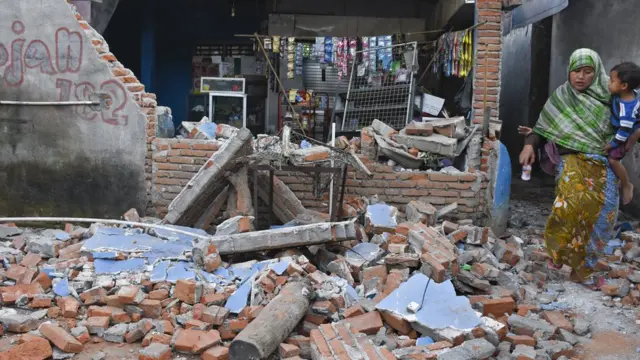 Seorang perempuan melintas dekat kios yang temboknya roboh pascagempa bumi di Dusun Lendang Bajur, Kecamatan Gunungsari, Lombok Barat, NTB, Senin (6/8).