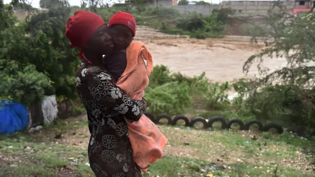 Mama ambeba mwanawe, wakati zoezi la kuhamisha raia likiendela kutokana na hatari ya mto ulio karibu kuvunja kingo zake, katika mji mkuu wa Haiti, Port-au-Prince, tarehe 4 , Oktoba 2016