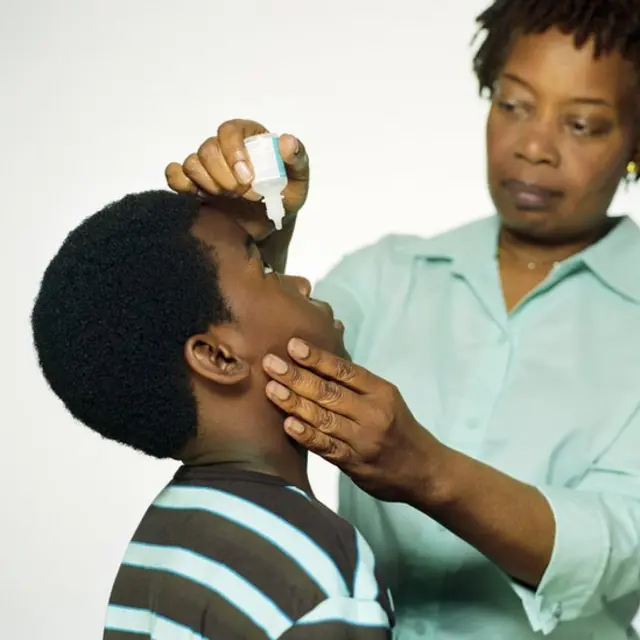 Mãe pinga colírio nos olhos do filho