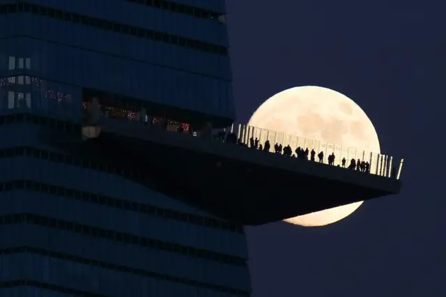 People standing on a large building platform are silhouetted by the moon