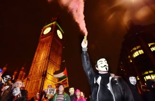 Masked protester (protestors, demonstrators), wearing a Guy Fawkes mask, demonstrates in front of the Houses of Parliament during the Million Mask March in Parliament Square on November 5, 2015