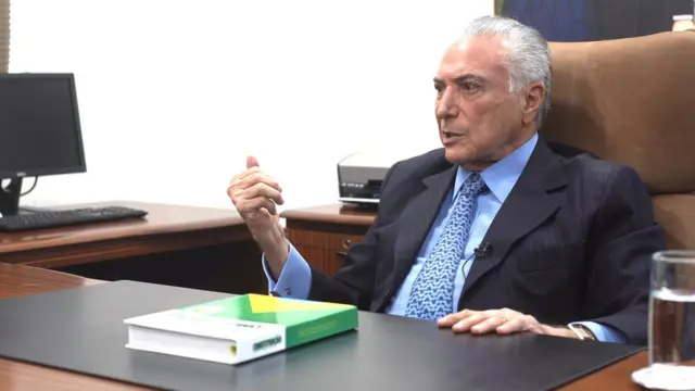 Temer dá entrevista sentadoapostas 365 betpoltrona e dianteapostas 365 betmesa no seu escritório, sobre a qual está um exemplar da Constituição