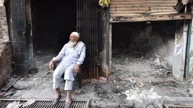 উত্তর-পূর্ব দিল্লিতে দাঙ্গায় পুড়ে ছাই হওয়া দোকানের সামনে বসে একজন ব্যবসায়ী