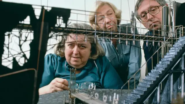 Dos mujeres y un hombre mirando una construcción en miniatura