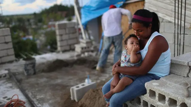 امرأة تجلس مع طفلها أمام منزلها الذي تهدم خلال إعصار ماريا