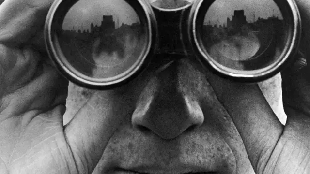 Un plano muy cercano de una persona mirando por unos binoculares, en una fotografía en blanco y negro