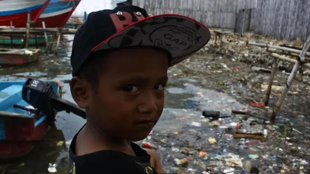 طفل يقف في مرسى للقوارب مليء بالمخلفات البلاستيكية