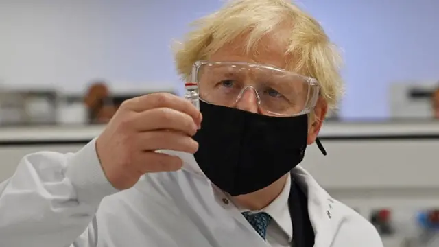 Foto do primeiro-ministro Boris Johnson com máscara segurando uma ampolavacina