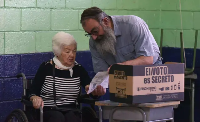 German Fainzildr ayuda a su madre Sara a votar en el centro electoral ubicado en la escuela primaria Carlos Sanabria de San José durante las elecciones generales de Costa Rica el 4 de febrero de 2018.