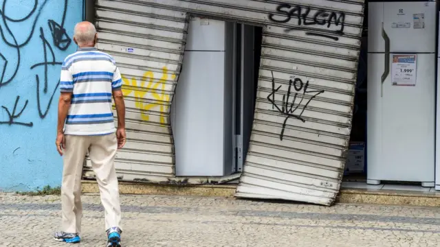 Homem observa porta arrombada durante saque a loja