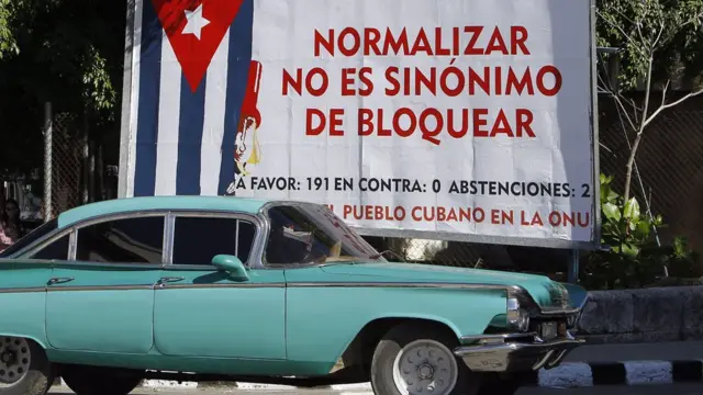 Un auto antiguo pasa frente a una valla en La Habana que denuncia el embargo económico