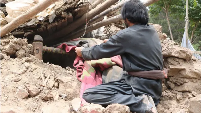 ভূমিকম্পে মাটির ঘরের ধ্বংস স্তূপ থেকে বিছানার অংশ বের করার চেষ্টা করা হচ্ছে।