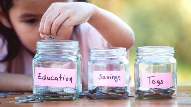 A child puts coins in different jars labelled education, savings and toys