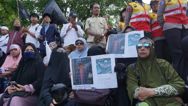 Massa yang berdemo membawa foto jalan yang dipotret dari atas untuk menegaskan bentuk mosaik itu menyerupai salib.