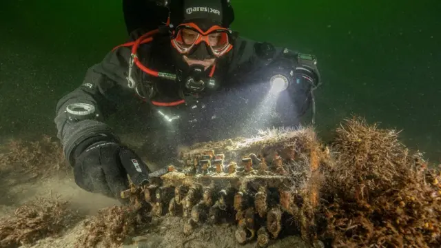 Un buzo junto a la máquina Enigma en el fondo del mar.