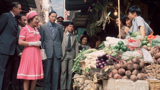 英国女王伊丽莎白二世（左二）在香港总督麦理浩爵士（Sir Murray MacLehose；左一）陪同下与中环嘉咸街某蔬菜摊摊主交谈（5/5/1975）