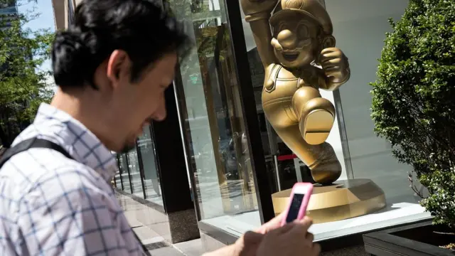 Estatua de Mario Bros frente a las oficinas de Nintendo. Un hombre pasa cerca, aparentemente jugando Pokemon Go.